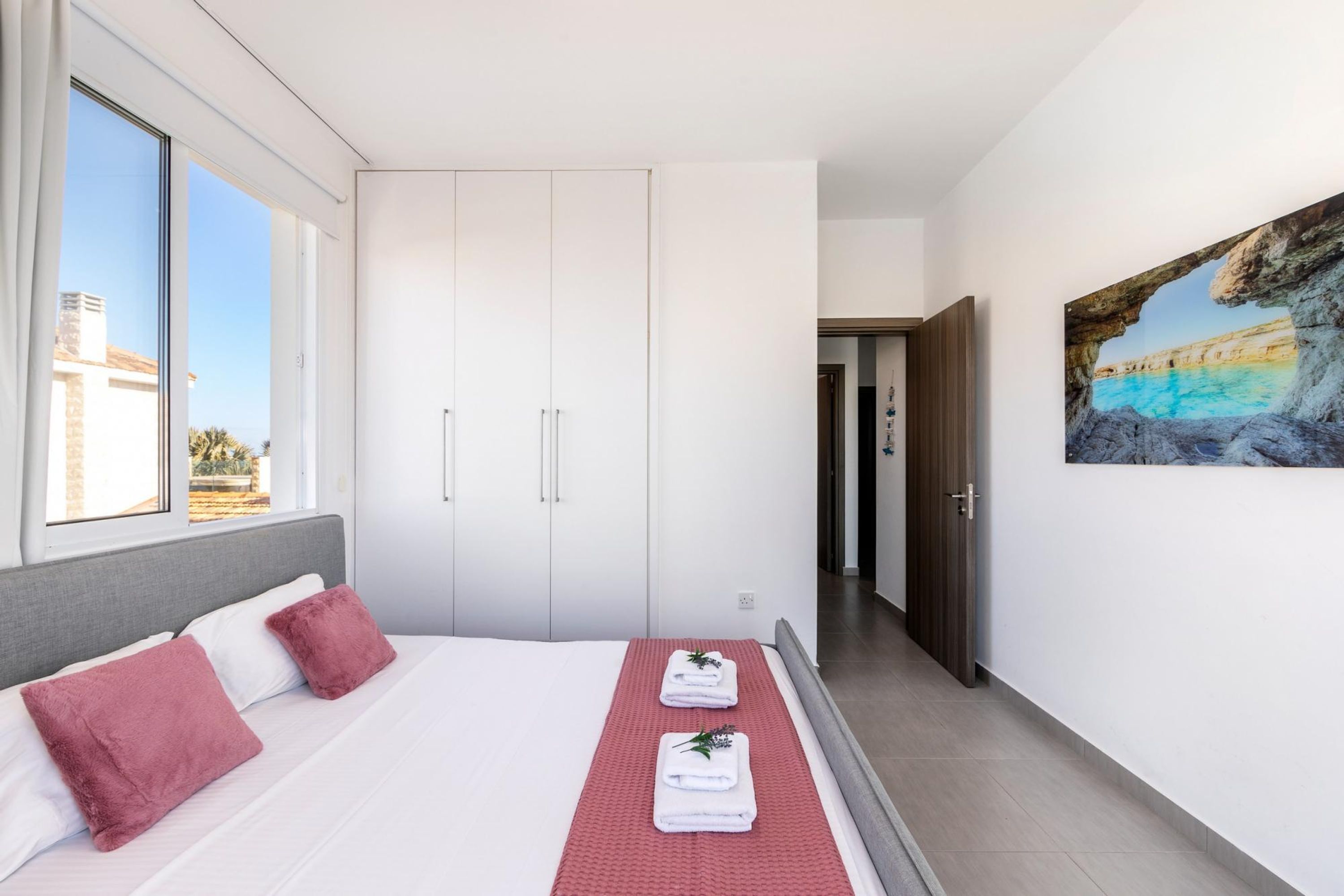 Ein modernes Schlafzimmer mit einem großen Bett, einem weißen Kleiderschrank und einem Gemälde mit einer Küstenlandschaft.