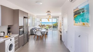 A modern kitchen with a washing machine, a dining area with a view of the sea, and a large painting on the wall. - Ayia Thekla Seafront Villa Dagi (Sotira)