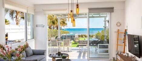 A modern living room with a view of the ocean, a dining area, and a TV on a wooden cabinet.