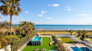 A pool area with a view of the sea, surrounded by palm trees and a white fence. - Ayia Thekla Seafront Villa Dagi (Sotira)