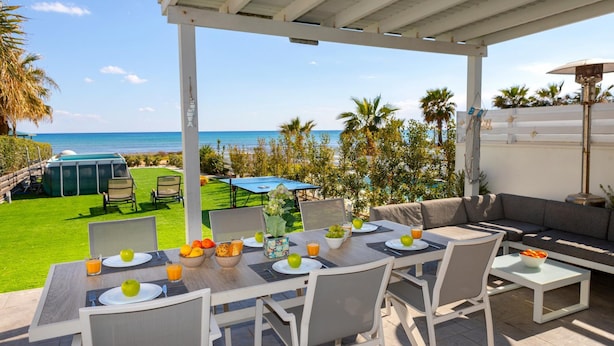 An outdoor dining area with a view of the beach, equipped with tables, chairs, and umbrellas. - Ayia Thekla Seafront Villa Dagi (Sotira)