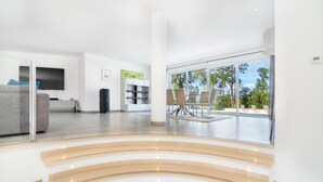 Een moderne woonkamer met een grijze bank, een flatscreen televisie, een boekenkast en een eethoek met stoelen.