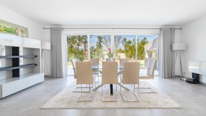 Een moderne eetruimte met een glazen tafel en stoelen, een witte console en uitzicht op de omgeving.