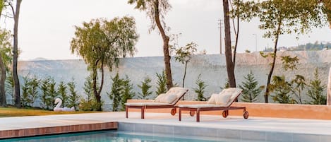 A pool area with two lounge chairs, a stone wall, and trees.