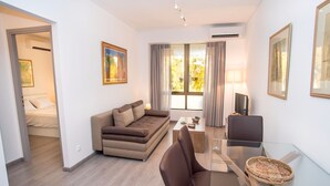 A modern living room with a sofa, a glass coffee table, and a TV. - Cozy Glyfada Getaway 1 bdr (Glyfada)