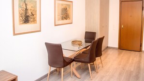 A dining area with a glass table, four chairs, two framed artworks on the wall, a wooden door, and a wooden floor. - Cozy Glyfada Getaway 1 bdr (Glyfada)
