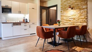 A modern kitchen with white cabinets, a built-in oven, and a dining area with a wooden table and orange chairs. - EVI Apartments - Valerie (Kaprun)