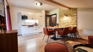 A modern kitchen with white cabinets, a microwave, and a dining area with a wooden table and orange chairs. - EVI Apartments - Valerie (Kaprun)