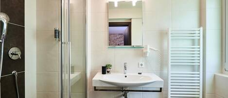 A modern bathroom with a glass shower enclosure, a white sink with a mirror above, and a white towel rack.