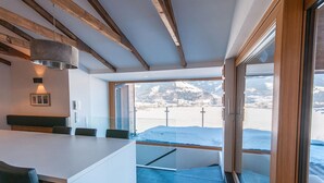 Un intérieur moderne doté d’une grande fenêtre offrant une vue sur les montagnes enneigées, d’un plafond en bois et d’un coin salon avec une table.