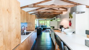 Une cuisine moderne avec des poutres en bois, un long plan de travail et une vue sur l’espace de vie.