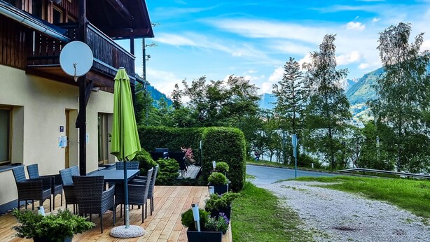 Eine Holzterrasse mit Gartenmöbeln, einer Satellitenschüssel und einem grünen Sonnenschirm.