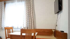 A room with a wooden table and chairs, a bench, a television mounted on the wall, and a window with curtains.