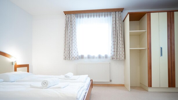 A hotel room with a bed, a window with curtains, a radiator, and a wardrobe.