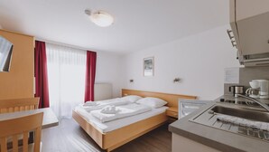 Ein Hotelzimmer mit Bett, Schreibtisch, Stuhl, einer Küchenzeile und einem Fenster mit Vorhängen.