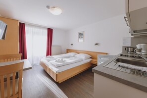 Une chambre d’hôtel équipée d’un lit, d’un bureau, d’une chaise, d’une kitchenette et d’une fenêtre avec des rideaux.