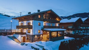A multi-story chalet with a stone facade, wooden balconies, and a ski slope in the background. - Chalet Evi in Kaprun (Kaprun)