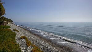 Una playa costera con un litoral rocoso, cielo despejado y mar tranquilo.