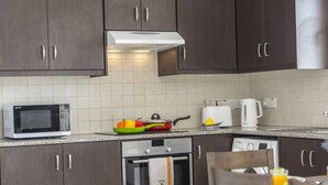 Een moderne keuken met donkere houten kastjes, een ingebouwde magnetron, een fornuis en een waterkoker op het aanrecht.