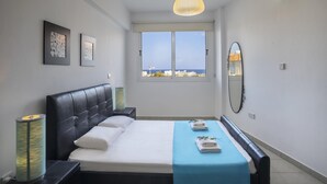 Een slaapkamer met een bed, nachtkastje, spiegel en foto's aan de muur, met uitzicht vanuit het raam.