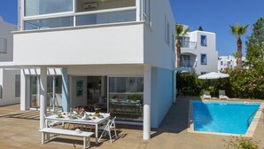 A modern two-story building with a pool, outdoor seating, and a clear view of the sky. - Protaras Villa Oceania (Paralimni)