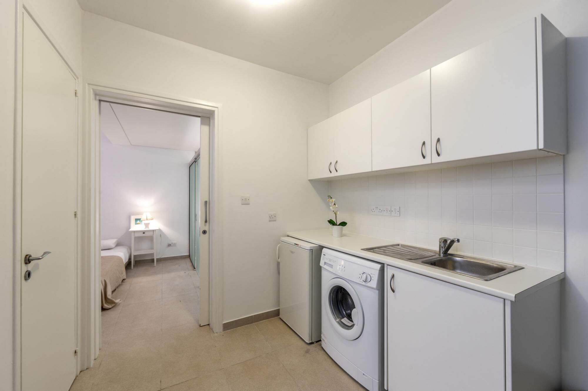 A compact kitchen with white cabinets, a washing machine, and a sink.