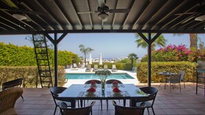 En overdækket terrasse med et bord dækket til to, der giver udsigt over en pool og et smukt landskab.