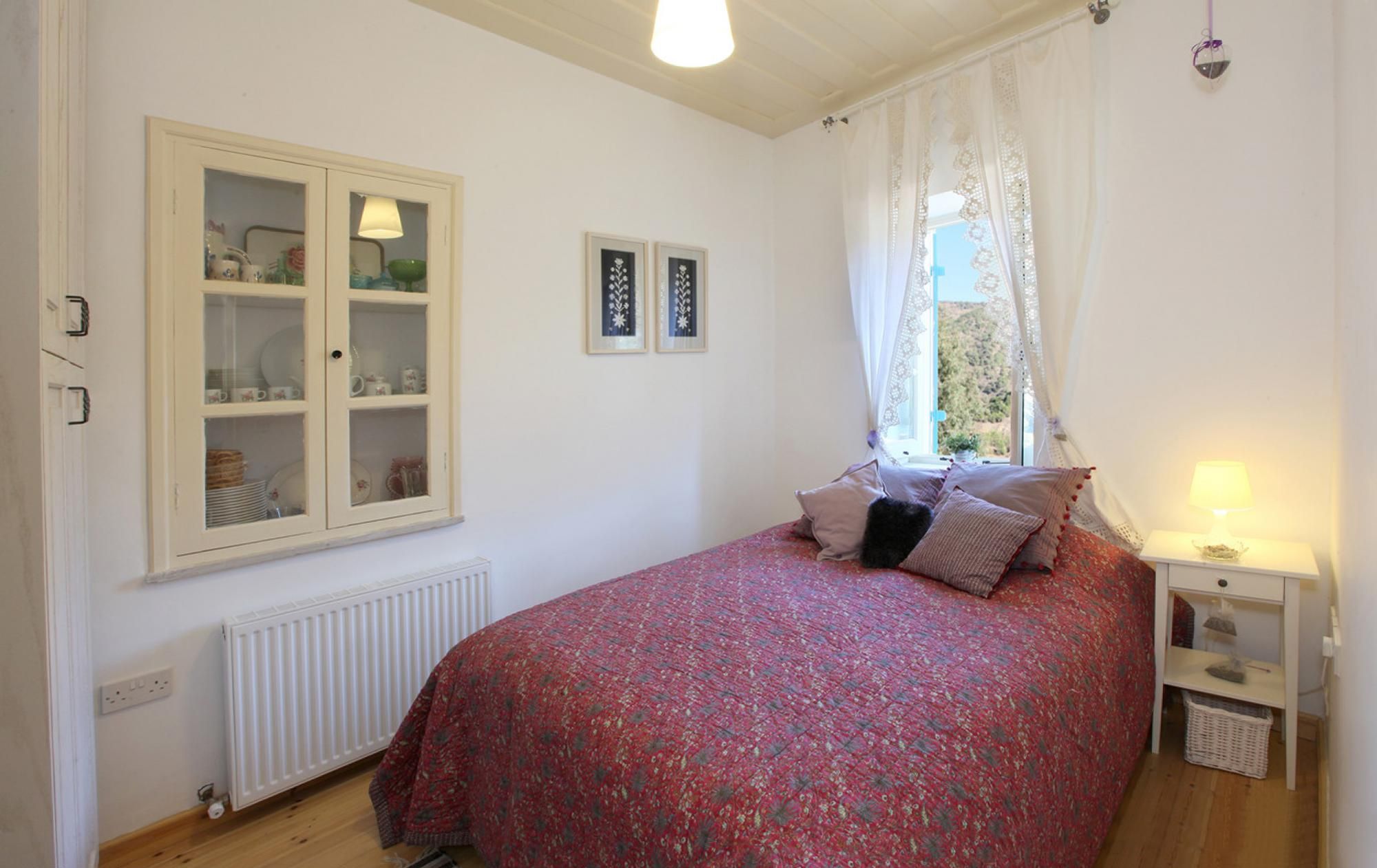 Cottage de tres habitaciones con cama, ventana con cortinas, radiador y aparador con puertas de cristal.