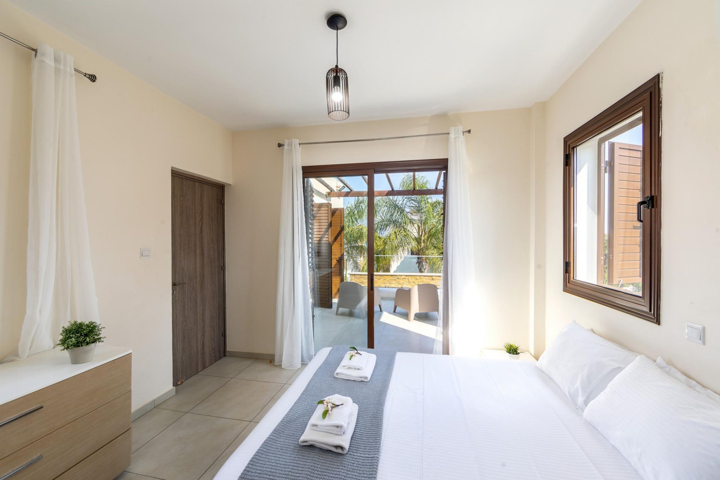 Une chambre à coucher comprenant un lit, une commode, une fenêtre et une porte donnant sur un balcon.