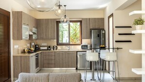A modern kitchen with wooden cabinets, stainless steel appliances, and a bar area with white chairs. - Ayia Napa Ionion Seaside Villa (Sotira)