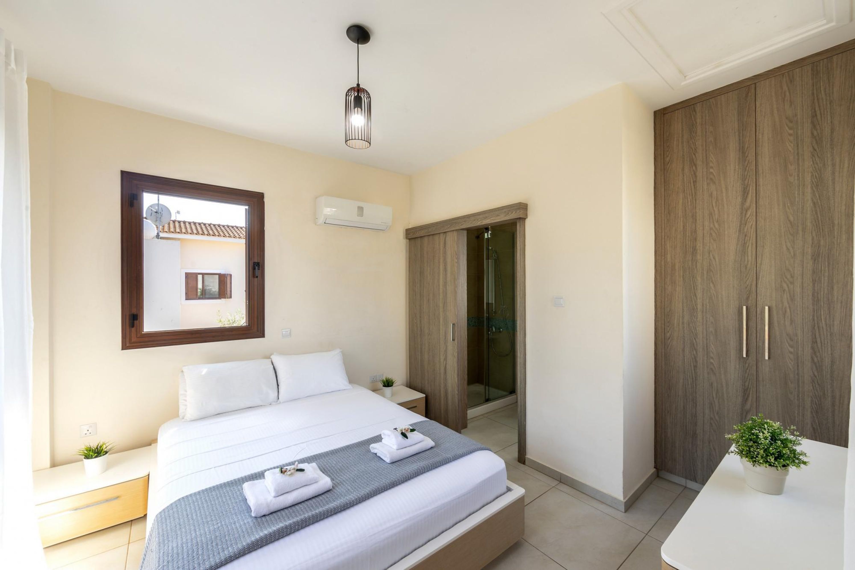 A modern bedroom with a bed, bedside table, mirror, wardrobe, and a shower area.