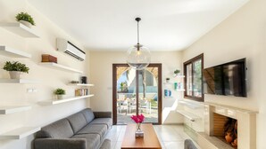 A modern living room with a grey sofa, a wooden coffee table, a TV mounted on the wall, and a fireplace. - Ayia Napa Ionion Seaside Villa (Sotira)