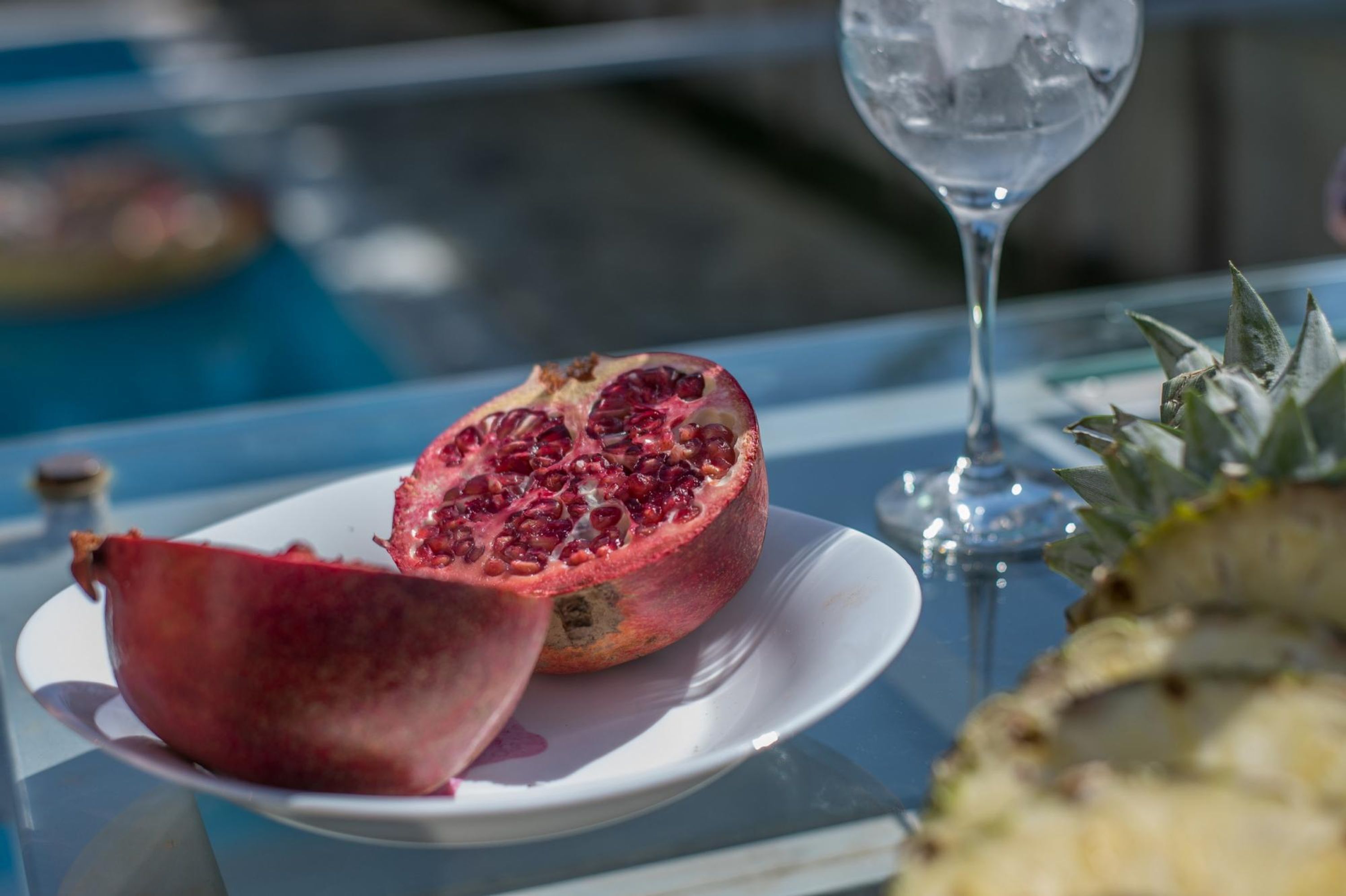 A pomegranate on a plate, a glass of water, and a pineapple on a table.