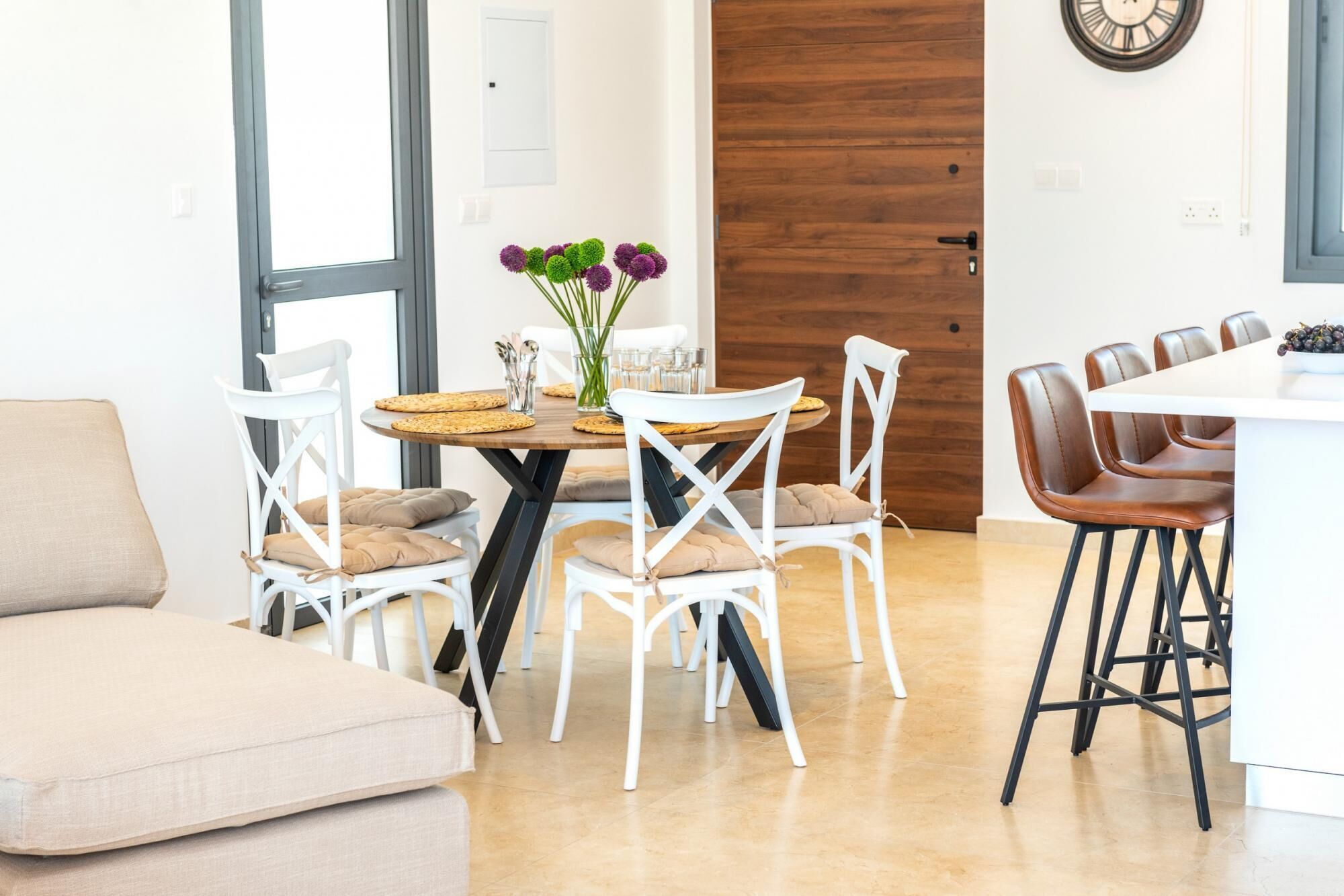 A modern dining area with white chairs, a wooden table, and a vase of flowers.