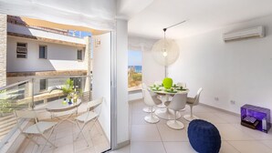 A modern apartment with a balcony, a dining area with white chairs, and a view of the sea. - Protaras Pallini Seaside Suite (Paralimni)
