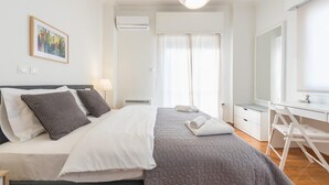 A bedroom with a bed, bedside table, lamp, and a desk with a chair. - Cozy and Fresh 2bdrm apt Close to Metro (Athens)