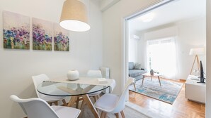 A modern dining area with a glass table, white chairs, and abstract wall art. - Cozy and Fresh 2bdrm apt Close to Metro (Athens)