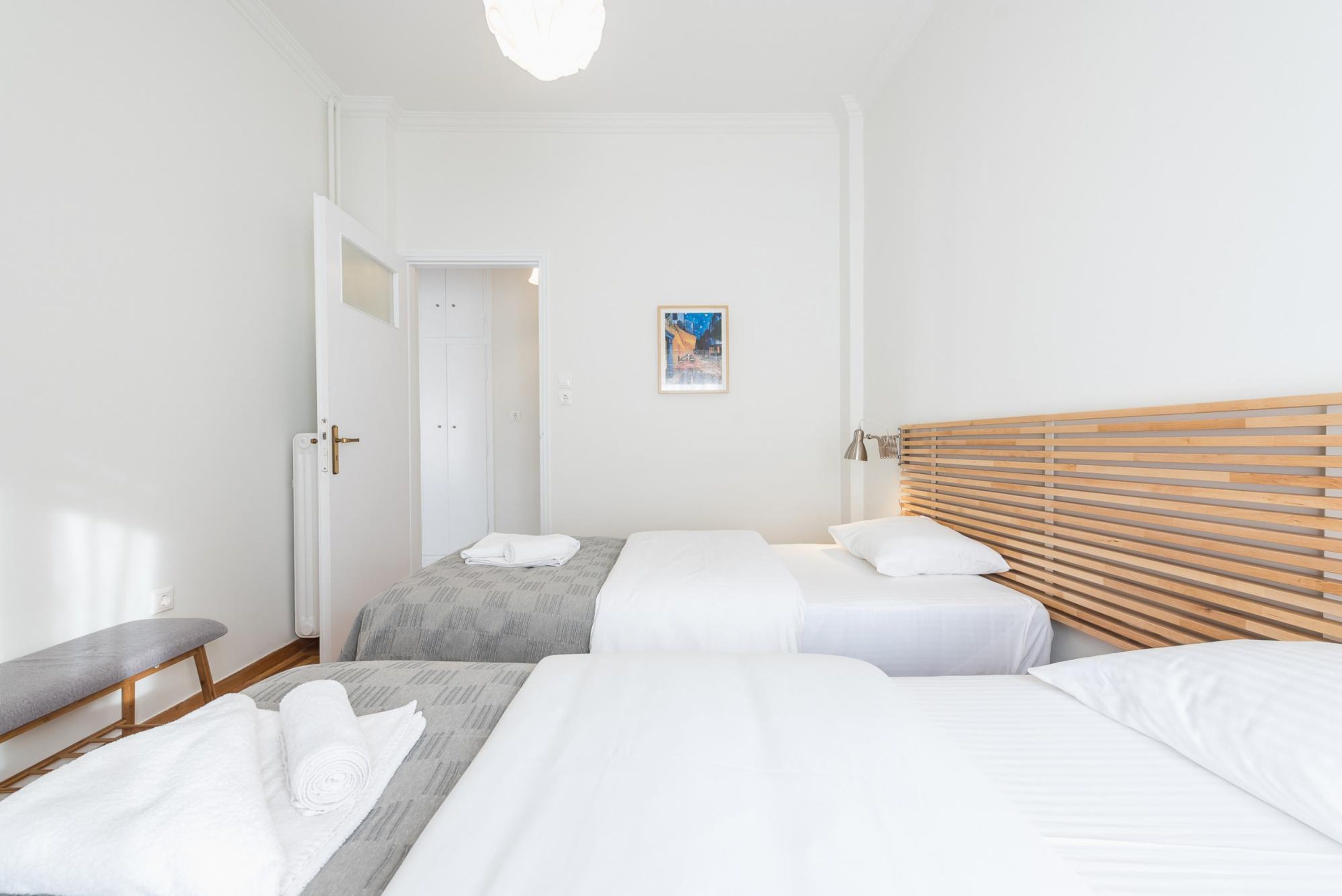 A hotel room with two beds, a bench, and a door leading to another room.