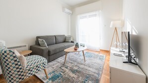 A modern living room with a grey sofa, patterned armchair, round coffee table, and a TV on a white stand. - Cozy and Fresh 2bdrm apt Close to Metro (Athens)
