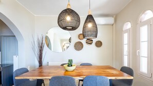 A dining area with a wooden table, six chairs, two hanging pendant lights, a mirror, and decorative wall pieces. - Voula Sea View Home With Jacuzzi Newly Refreshed 2026 (Vari-Voula-Vouliagmeni)
