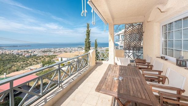 A terrace with a wooden table and chairs, a view of the sea and city, and a lattice fence. - Voula Sea View Home With Jacuzzi Newly Refreshed 2026 (Vari-Voula-Vouliagmeni)