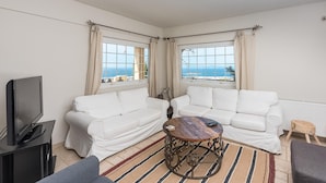 A living room with two white sofas, a wooden coffee table, a television, and a view of the sea through large windows. - Voula Sea View Home With Jacuzzi Newly Refreshed 2026 (Vari-Voula-Vouliagmeni)