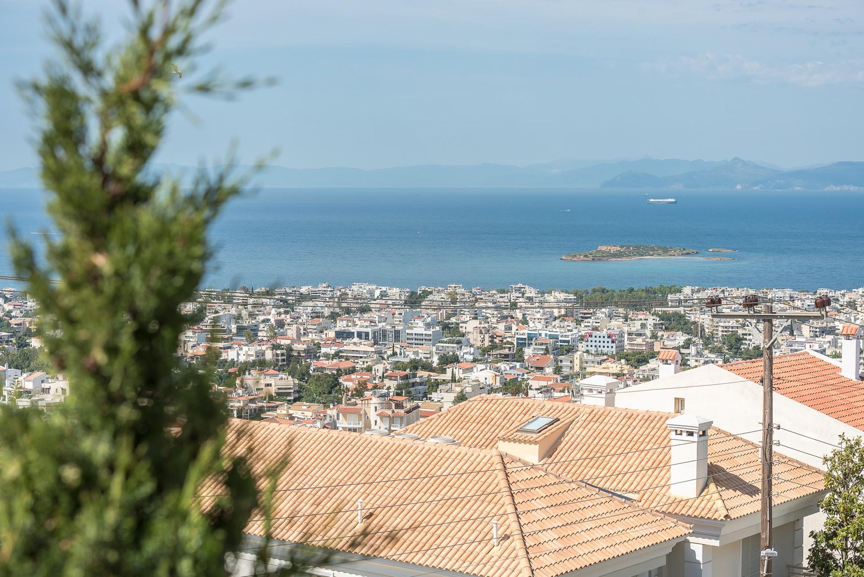 A coastal cityscape with a view of the sea and distant mountains.