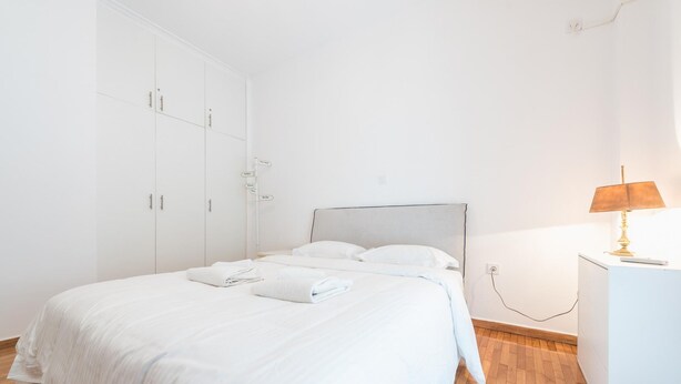 A bedroom with a bed, white wardrobe, and a bedside table with a lamp. - Fresh and Clean apt for 6 in Koukaki (Athens)