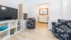 A modern living room with a flat-screen TV, floral-patterned armchairs, a white console table, and a small side table. - Fresh and Clean apt for 6 in Koukaki (Athens)