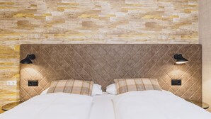 A bed with a quilted headboard, two bedside lamps, and a stone-patterned wall. - Alpine City Living - TOP 13 (Zell am See)