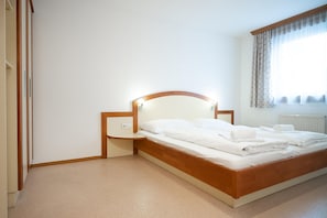 A neatly made bed with white linens and a wooden headboard, a bedside table with a lamp, and a window with curtains. - Seilergasse Apartments - TOP 8 (Zell am See)