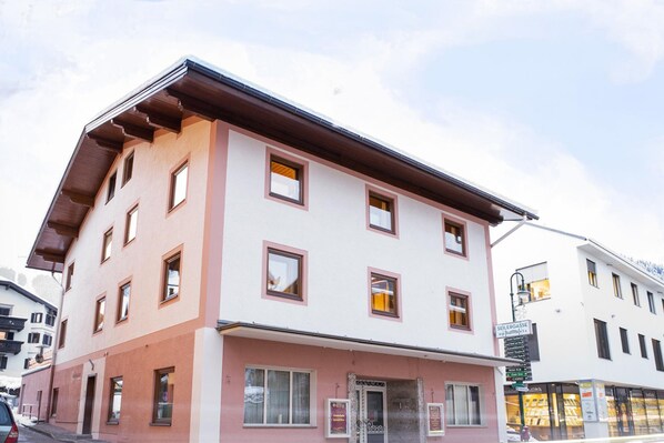 Un edificio de varios pisos con fachada rosa y blanca, múltiples ventanas y una entrada visible.