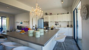 A modern kitchen with a central island, white cabinets, and a chandelier. - Aster Suite in Protaras (Paralimni)