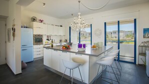 A modern kitchen with a central island, white cabinetry, and a large window offering a view. - Aster Suite in Protaras (Paralimni)